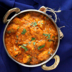 Paneer butter masala served in a siver dish, on a blue background