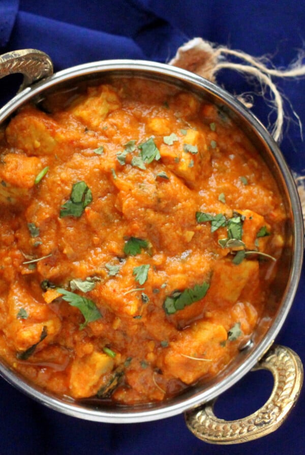 Paneer butter masala served in a siver dish, on a blue background