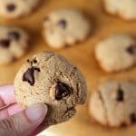 Chocolate chip cookies on a work surface with one being held up towards camera