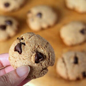 Chocolate chip cookies on a work surface with one being held up towards camera
