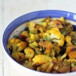 Vegan aloo gobi in a blue rimmed bowl on a white marble worktop