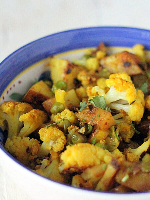 Vegan aloo gobi in a blue rimmed bowl on a white marble worktop