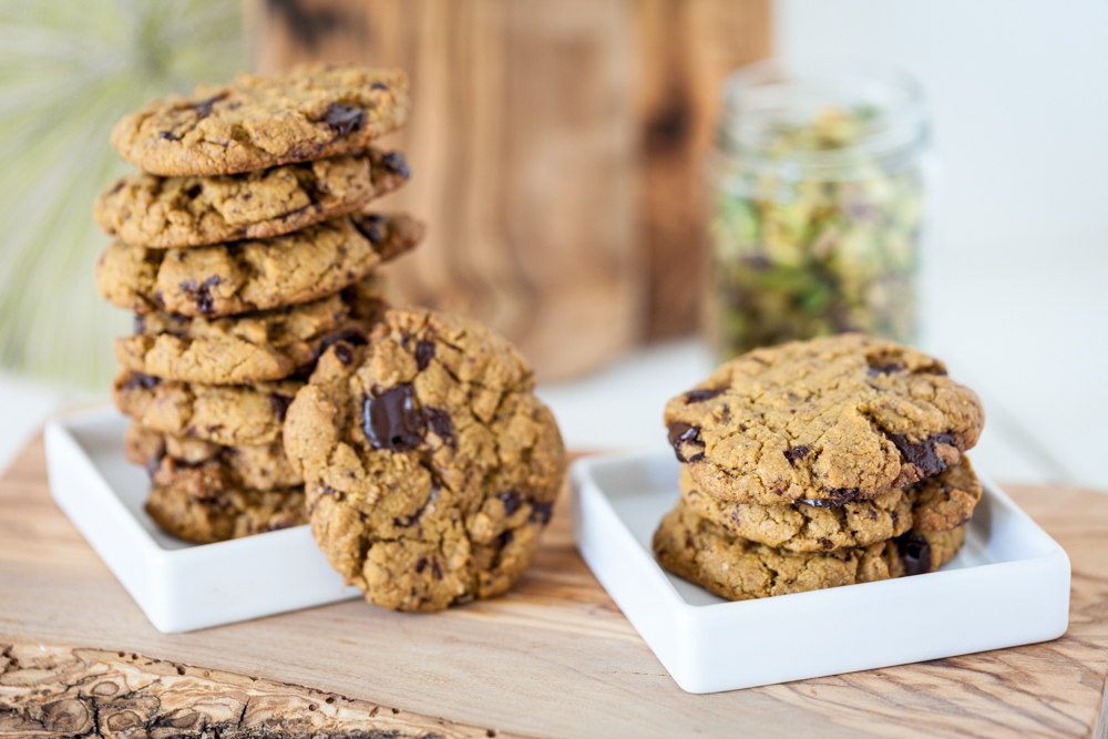 An easy Pistachio Cookies recipe with pistachio butter as the main ingredient and chocolate chunks for extra good flavor! Vegan, Gluten Free. stack of chocolate chunk pistachio cookies on two white plates on wooden board