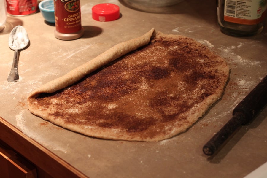 vegan cinnamon rolls  rolled out and filled cinnamon roll dough being rolled up to shape buns