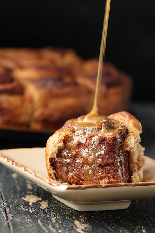 vegan cinnamon rolls  side view of a homemade fluffy and soft vegan cinnamon roll being drizzled with maple icing