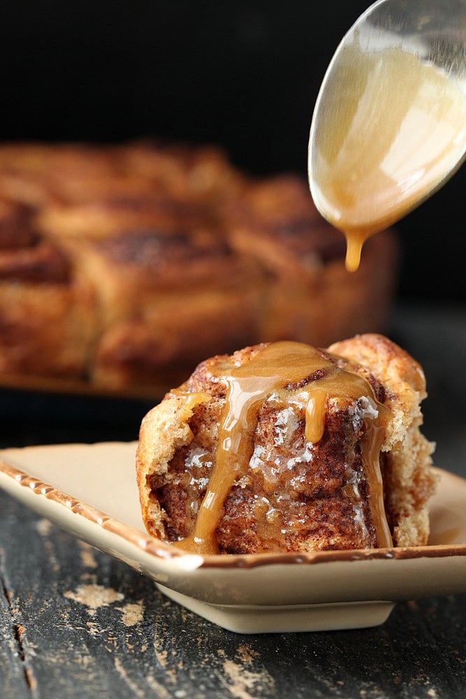 vegan cinnamon rolls  maple coffee icing being drizzled on top of vegan cinnamon rolls