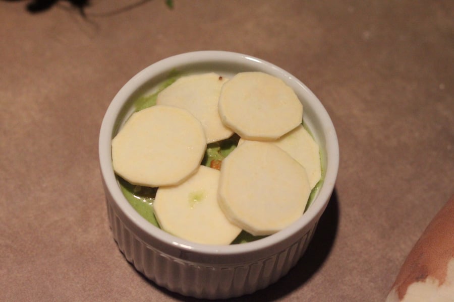 alfredo bake white sweet potatoes, spinach alfredo sauce and bell pepper being layered in a casserole dish to make alfredo bake