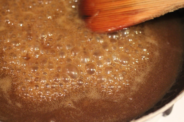 salted caramel brownies a wooden spoon stirring in a sauce pan with vegan salted caramel sauce