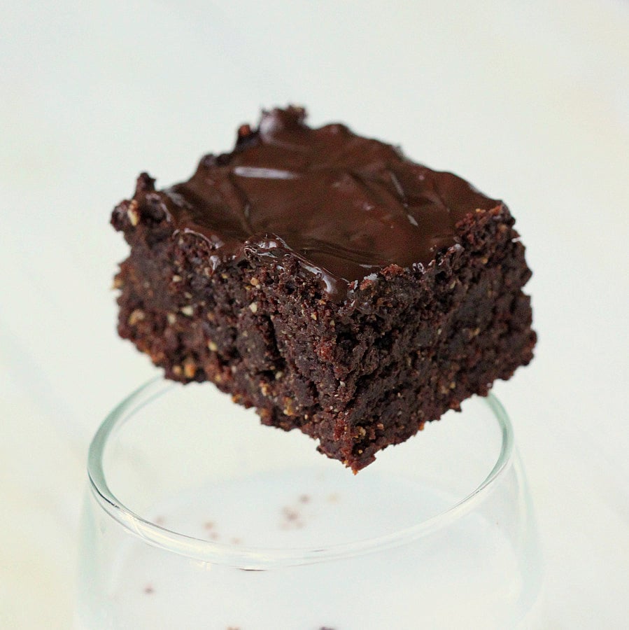 Salted Caramel Brownies a small Vegan Triple Chocolate Salted Caramel Brownie balancing on the rim of a milk glass