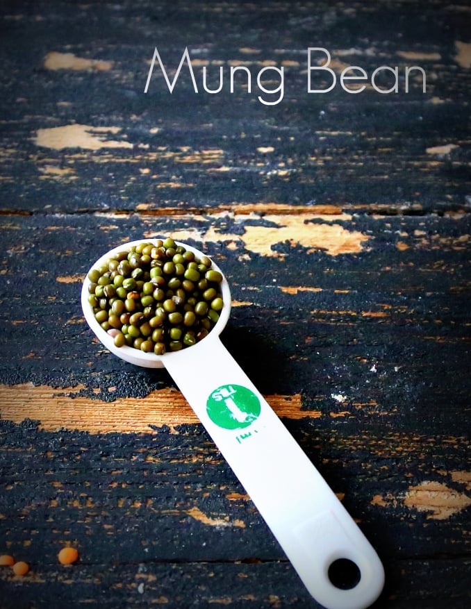 mung dal a white plastic teaspoon with mung beans on a black wooden table