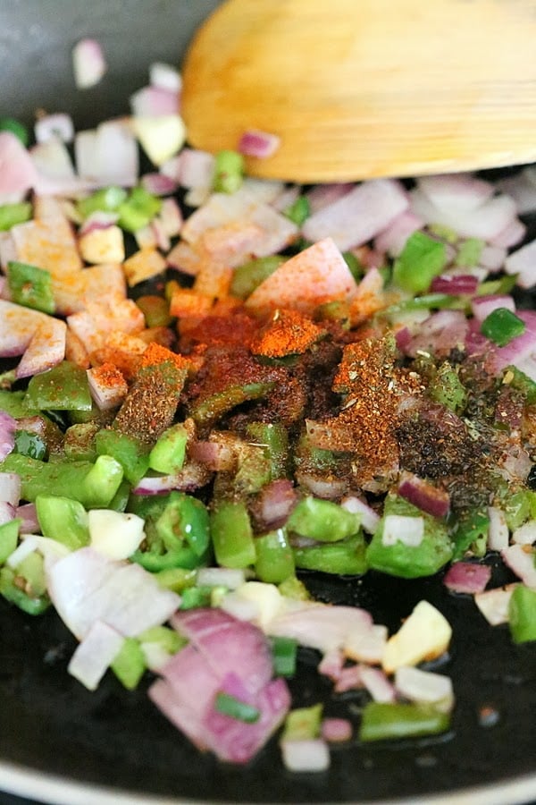 vegan wrap recipe chopped onion, bell peppers, chili and garlic powder being sauteed in a black pan