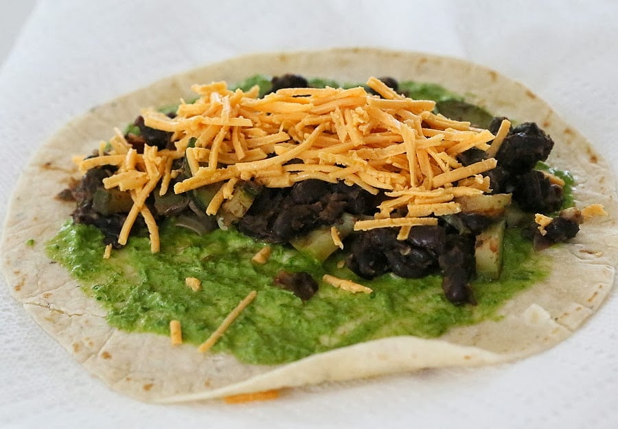 vegan wrap recipe a wheat wrap being topped with chimichurri, black beans and vegan shredded cheese