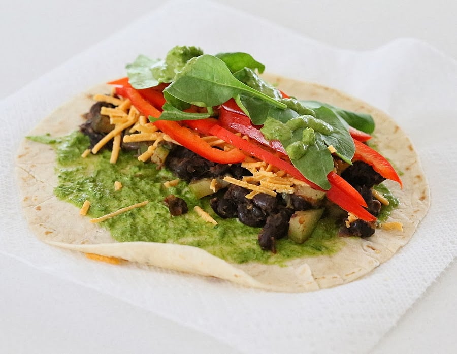 vegan wrap recipe a wheat tortilla wrap topped with black beans, spinach and dairy-free cheese