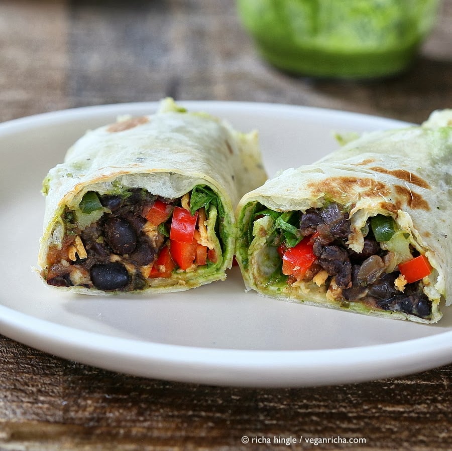 vegan wrap recipe a halved healthy vegan wrap with smoky black beans, spinach, chimichurri and vegan cheese on a white plate