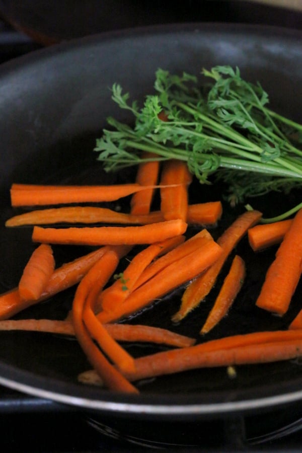 kale salad recipe  carrot sticks and carrot greens sauteeing in a black pan