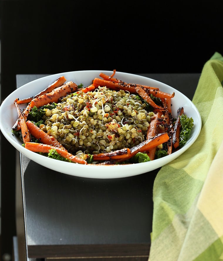 kale salad recipe  side view of a bowl of kale salad topped with sprouted mung beans and seared carrots