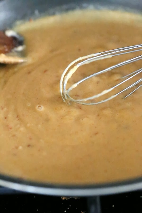 Cajun mac and cheese vegan mac and cheese sauce being stirred with a metal whisk in a saucepan