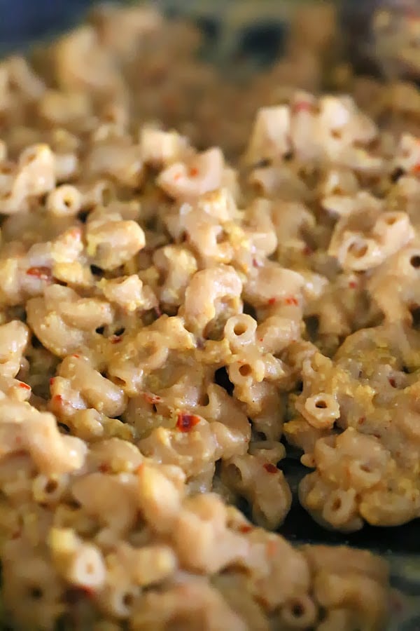 Cajun mac and cheese whole wheat elbow pasta being tossed with dairy-free cheese sauce to make vegan mac and cheese