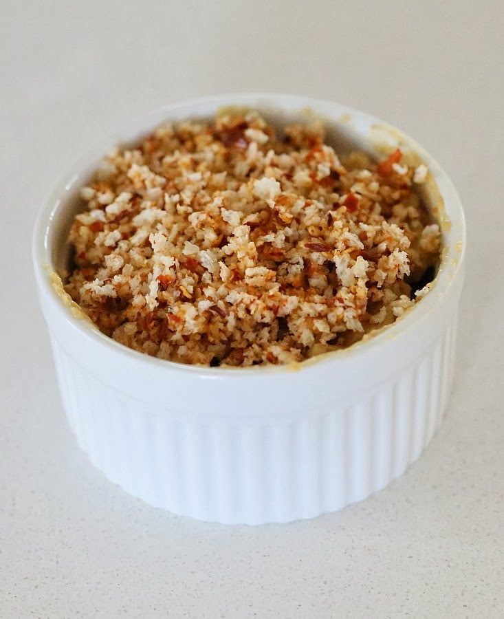 Cajun mac and cheese individual ramekins with dairy-free spicy mac and cheese being filled topped with vegan breadcrumbs