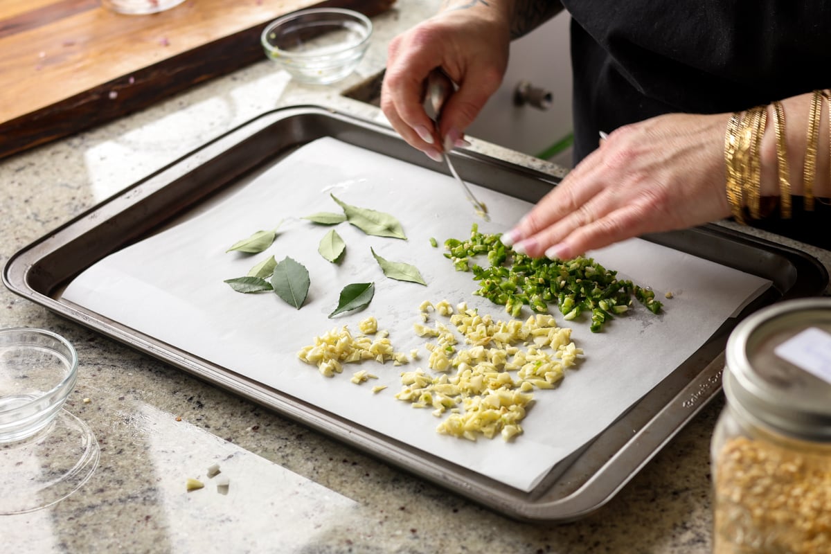 spreading curry leaves, garlic, and chili onto the baking sheet