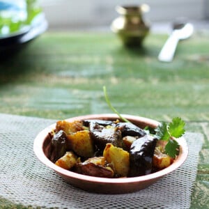 A plate of Ringan Batata Nu Shaak on a green background with a green herb sprig