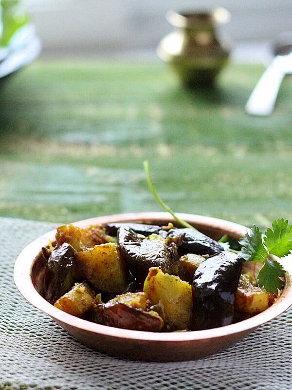 A plate of Ringan Batata Nu Shaak on a green background with a green herb sprig