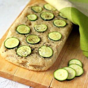 A loaf of Gluten-free Zucchini Basil Focaccia on a cutting board with slices of zucchini next to it