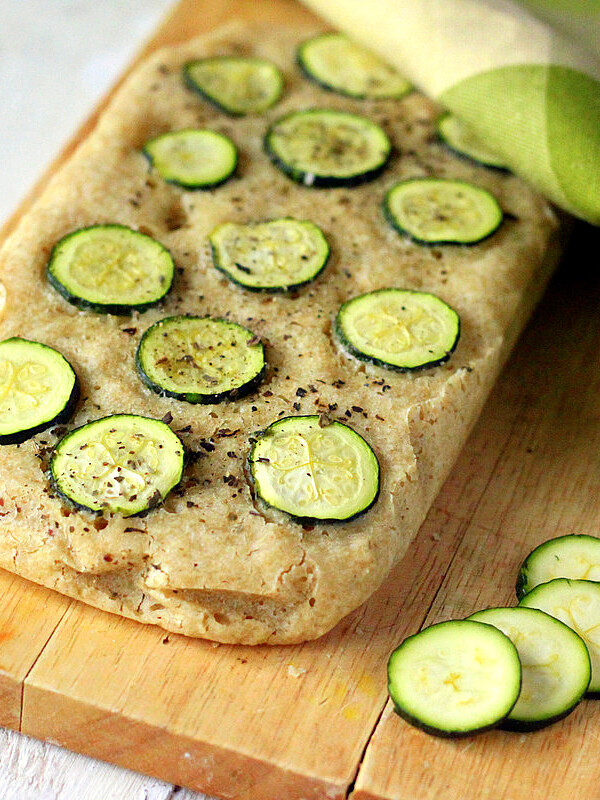 A loaf of Gluten-free Zucchini Basil Focaccia on a cutting board with slices of zucchini next to it