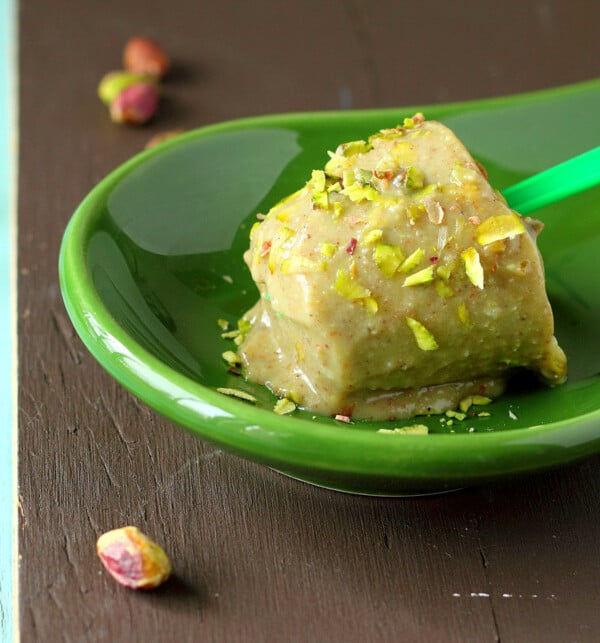 A pistachio kulfi icecream popsicle on a green plate