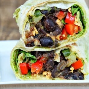 a healthy vegan wrap cut in half revealing a black bean and spinach filling