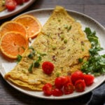 chickpea omelet on a plate with orange slices and tomato