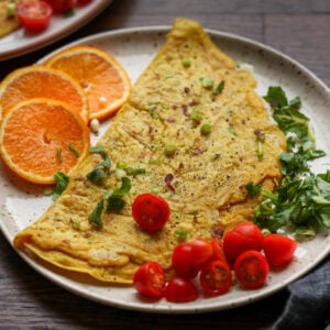chickpea omelet on a plate with orange slices and tomato