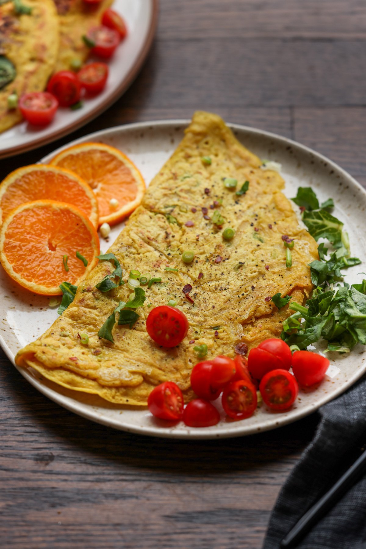 chickpea omelet on a plate with orange slices and tomato