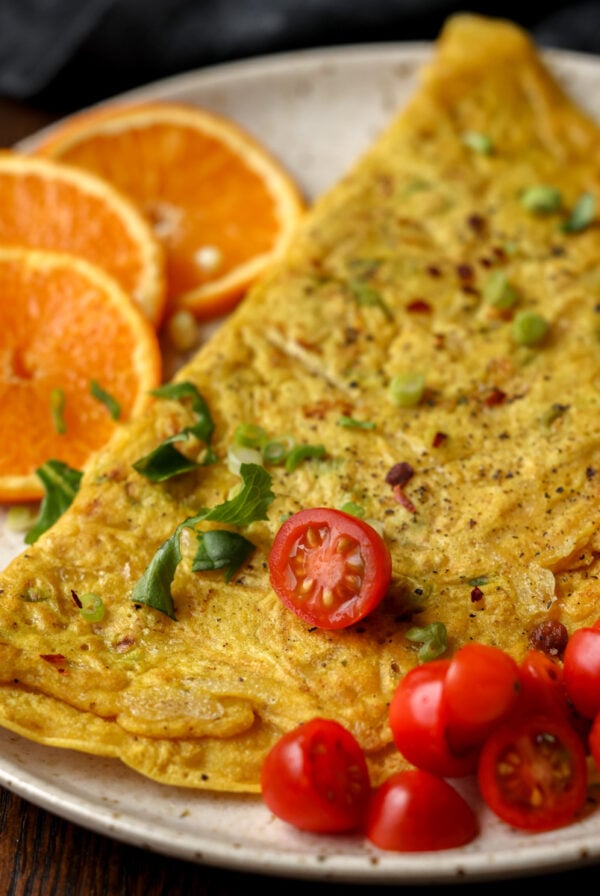 chickpea omelet on a plate with orange slices and tomato