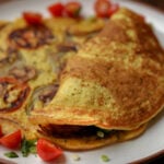 chickpea omelette with veggies inside next to one prepared with the fillings stuffed into the folded omelet