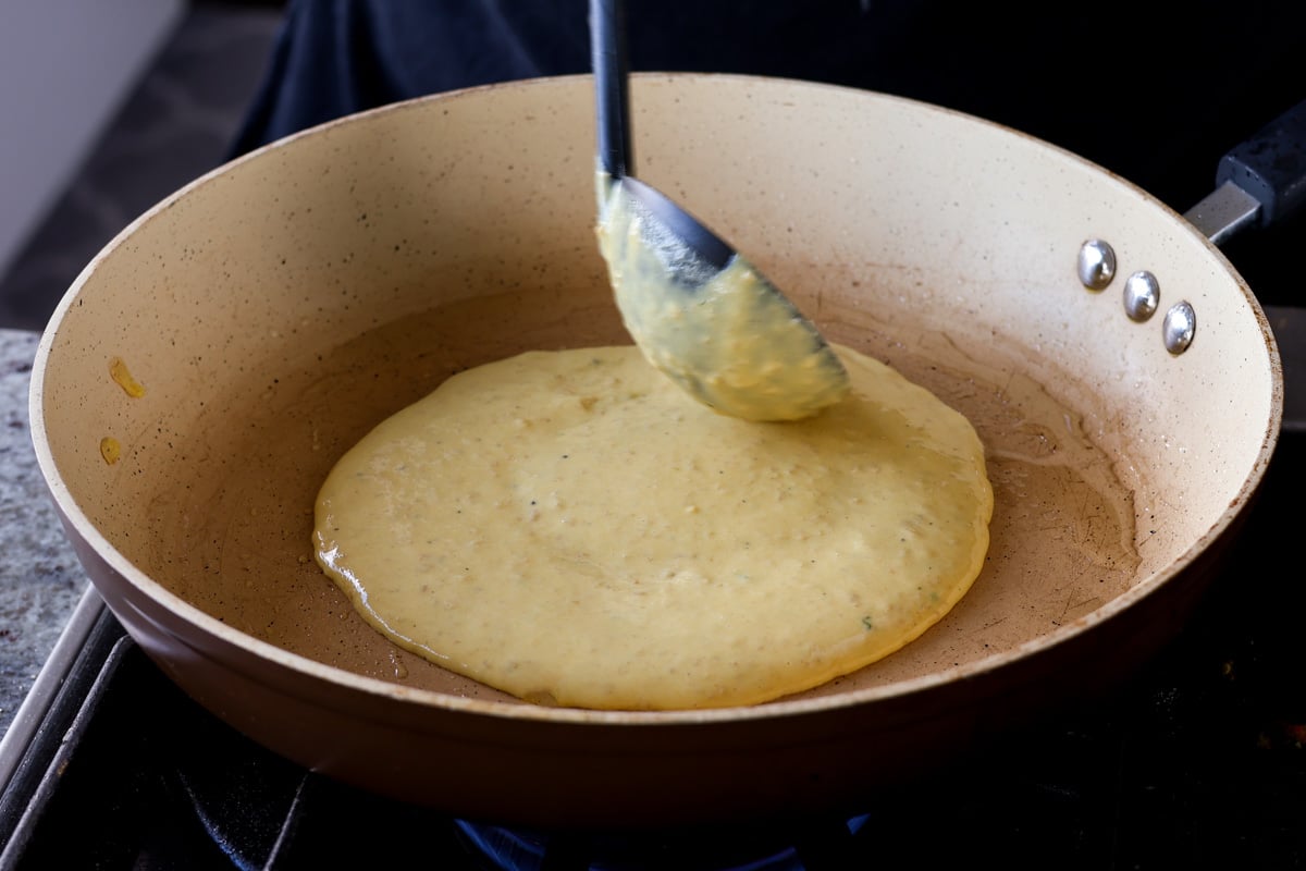 ladling vegan omelet batter into a hot pan