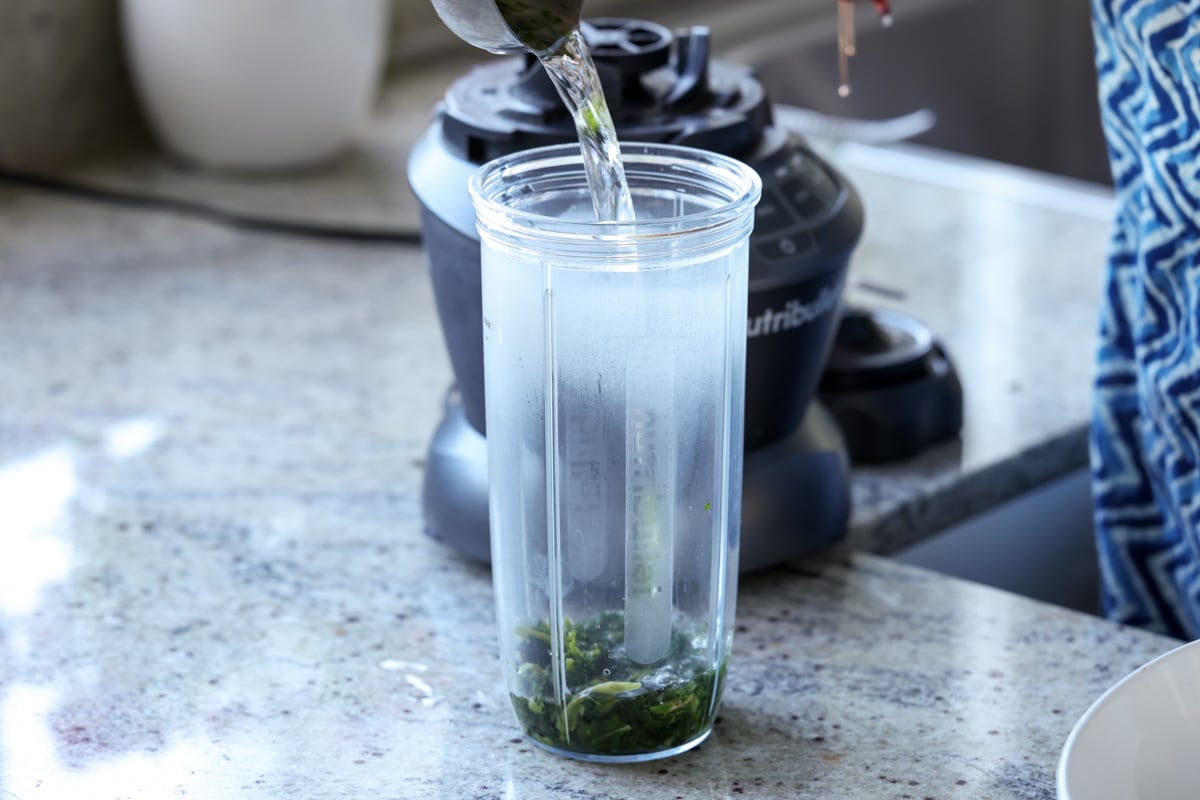 adding spinach and water to the blender