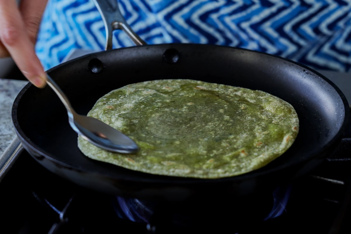 pressing the paratha with a spoon