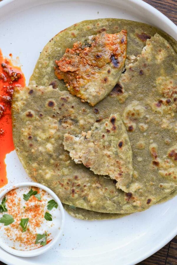 spinach paratha on a plate with raita and Indian pickle