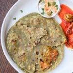 spinach paratha on a plate with raita and Indian pickle