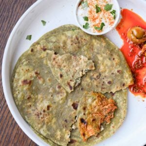 spinach paratha on a plate with raita and Indian pickle