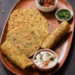 methi thepla on a serving tray with raita, Indian pickle, and chutney