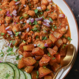 close-up of chana masala in the bowl with the crispy potatoes, rice, and cucumber