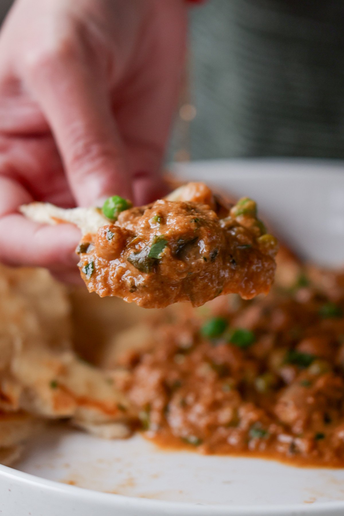 hand scooping up mushroom matar masala onto a piece of flatbread