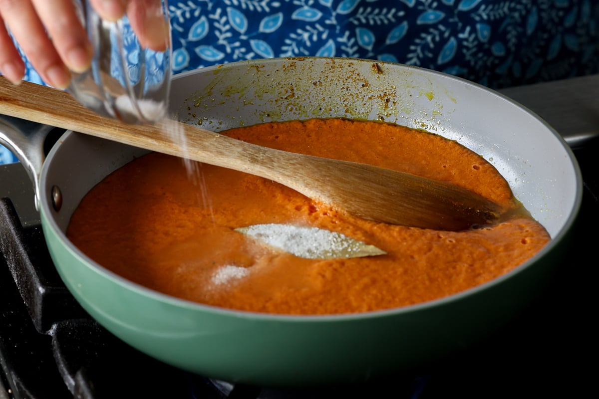 adding bay leaf and salt to the spiced tomato soup
