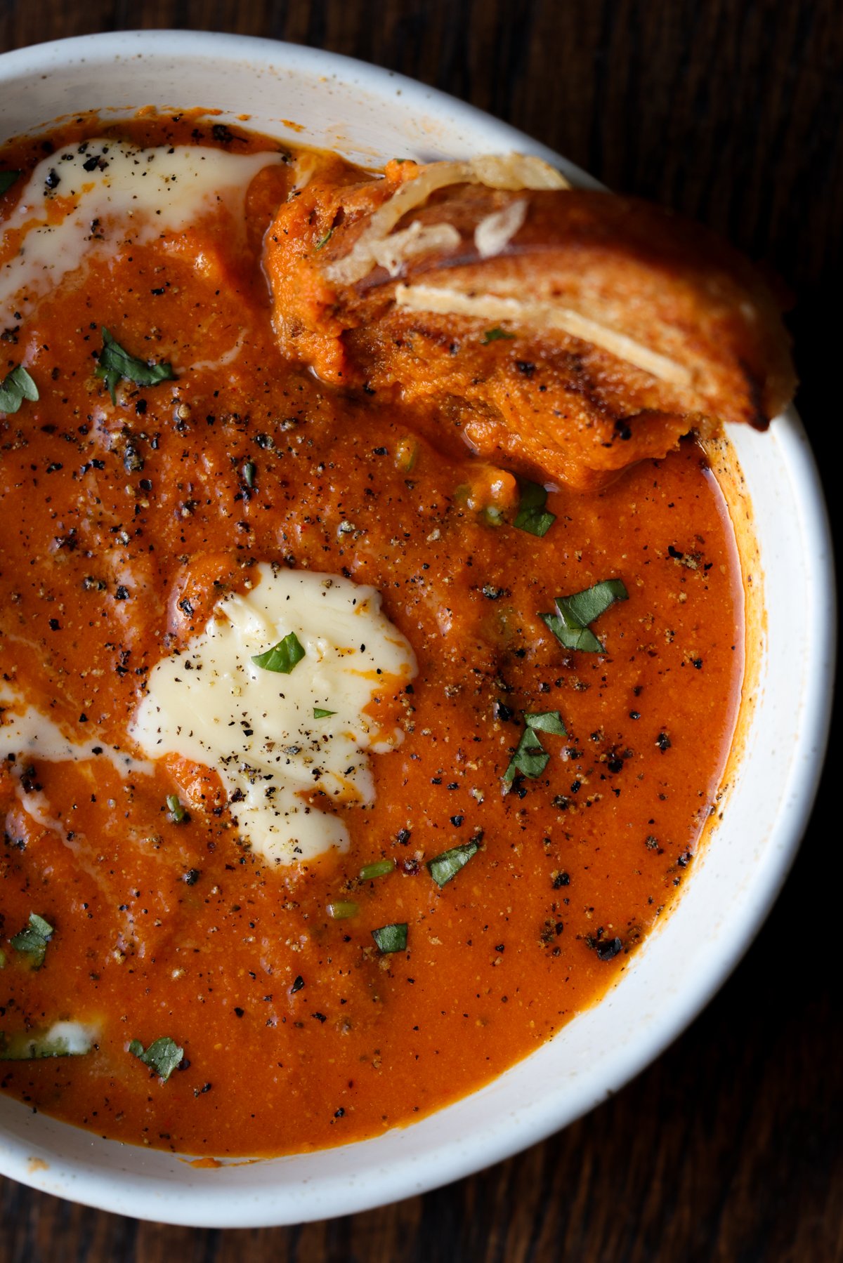 bowl of spiced tomato soup with garnishes added the grilled cheese