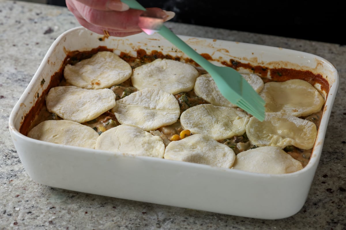 brushing pastry wash onto the veggie pot pie topped with puff pastry cutouts