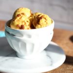 Scoops of vegan mango ice cream in a white bowl on a wooden worktop