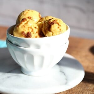 Scoops of vegan mango ice cream in a white bowl on a wooden worktop