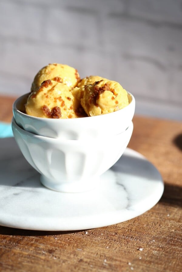 Scoops of vegan mango ice cream in a white bowl on a wooden worktop